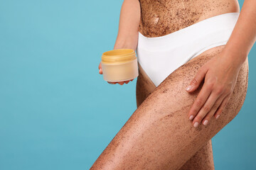 Woman with body scrub on her skin and jar against light blue background, closeup. Space for text