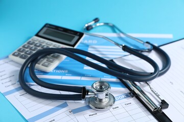 Stethoscope, calculator and medical card forms on light blue background, closeup