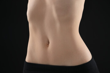 Naklejka premium Attractive woman against black background, closeup on belly