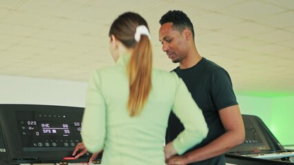 Fitness instructor assisting client setting up treadmill for training, demonstrating professionalism and dedication to client's workout goals in modern gym setting.African american personal trainer