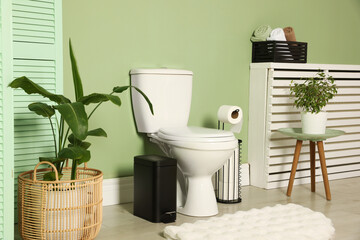 Ceramic toilet bowl, houseplants and necessities near green wall indoors