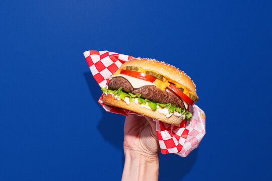 Hand holding a classic cheeseburger against a blue background