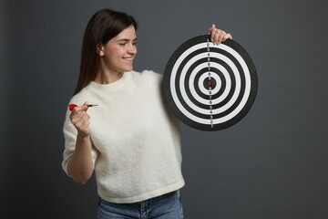 Targeting. Smiling woman with dart board and arrow on grey background