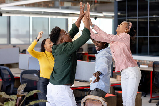 In modern office, team celebrating success with high-fives and smiles
