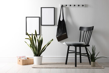 Empty picture frames on white wall, string bag, chair and houseplants indoors