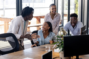 African American team collaborating and laughing around computer in modern office
