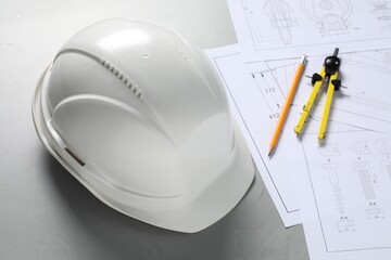 Different engineering drawings, hard hat, pencil and divider on grey table, above view