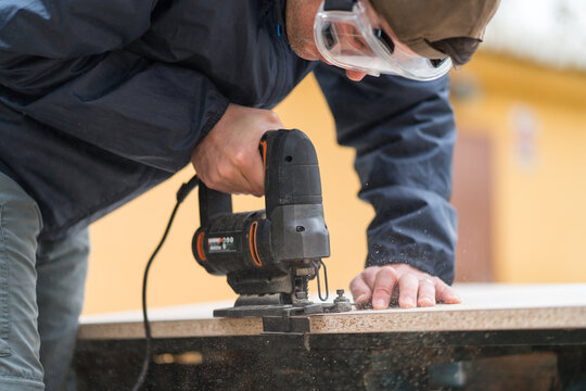 Anonymous man using jigsaw for carpentry outdoors