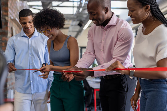Diverse team cutting red ribbon at office opening, celebrating new beginnings