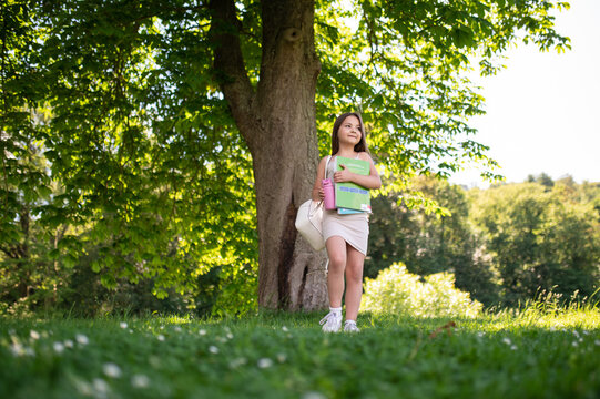 Child walking in park with backpack and bools in hands book on sunny day