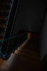 A dimly lit wooden staircase with an intricate iron railing descends into shadow. The interplay of...