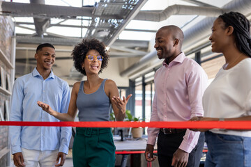 Colleagues celebrating office opening, smiling and talking near red ribbon indoors
