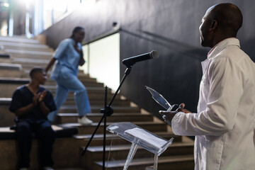 African American doctor presenting at podium while colleagues listen on staircase