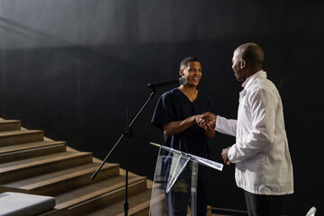 Two men shaking hands on stage, smiling and engaging in conversation