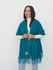 Smiling woman with long dark hair wearing a teal shawl draped over a white turtleneck. The shawl...