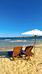 Mobile photo of picturesque beach scene featuring lounge chairs and umbrellas. The clear blue sky and gentle waves offer a perfect backdrop for a day of relaxation by the sea