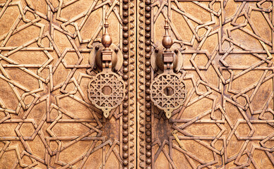 Finely engraved brass door in Moorish style, adorned with geometric patterns and traditional knockers, in Fez, Morocco.