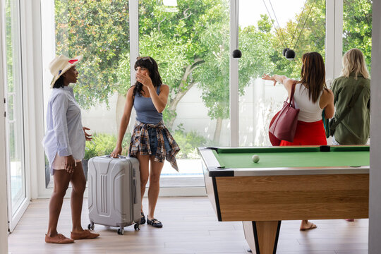 Women arriving at vacation home with luggage, exploring bright living room