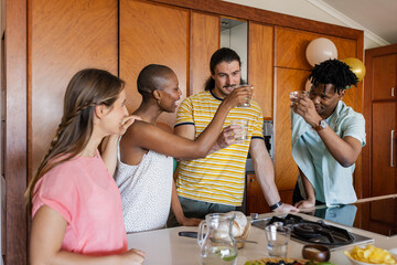 Friends toasting with drinks in modern kitchen, enjoying casual gathering together