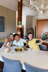 Friends taking selfie at home, celebrating with food and drinks, smiling joyfully