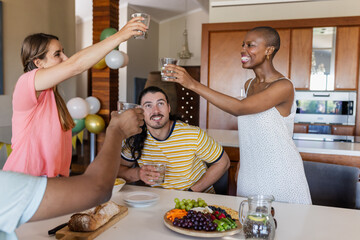 Friends celebrating at home, raising glasses around table with fruits and bread