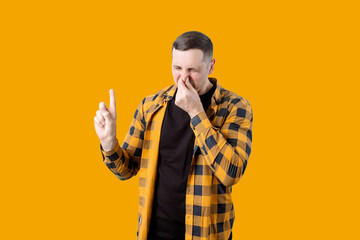 Young man covers his nose from a bad smell on a yellow background. Isolated portrait. People and emotions