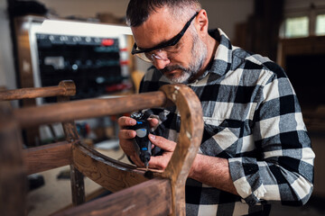 Carpenter standing in his workshop restoring old piece of furniture with mini grinder.