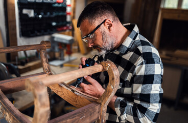 Carpenter standing in his workshop restoring old piece of furniture with mini grinder.