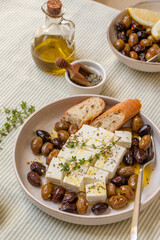 Freshly prepared feta cheese served on a plate with assorted olives, garnished with herbs and lemon slices and  crusty bread, traditional Greek or Italian food, Mediterranean diet