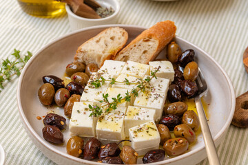 Freshly prepared feta cheese served on a plate with assorted olives, garnished with herbs and lemon slices and  crusty bread, traditional Greek or Italian food, Mediterranean diet