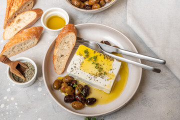 Fresh feta cheese with olives, olive oil and herbs with fresh bread, traditional Greek or Italian food, Mediterranean diet