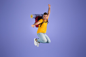 Obraz premium Excited young Caucasian tourist with camping equipment jumping on blue studio background. Full length portrait of funky guy thrilled over his summer holiday camping trip