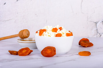 Fototapeta premium Fresh cottage cheese with dried apricot pieces and honey in a white bowl.
