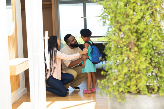 Parents helping daughter with backpack, preparing for school at home