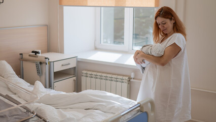Caucasian woman holding newborn son in maternity hospital ward. 