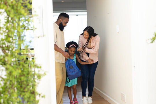 Parents helping daughter with backpack, preparing for school in hallway
