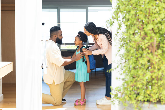 Parents helping daughter with backpack, preparing for school at home, smiling warmly
