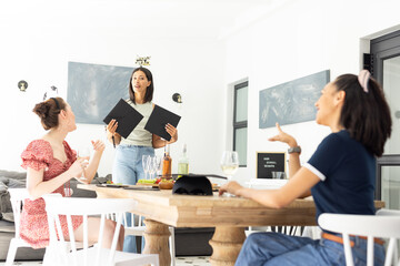 Holding menus and smiling, young woman with Birthday Girl headband stands by table