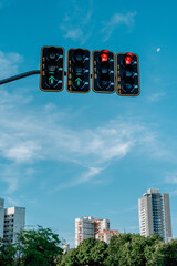 Red traffic lights under clear blue sky with visible moon