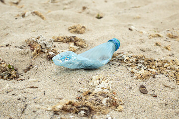 A plastic bottle on the beach in the sand and seaweed, which was thrown out of the sea by a storm. It spoils the ecology!