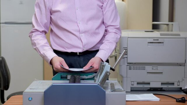 A man uses a paper cutter and binding machine in an office setting to process documents with precision