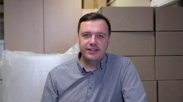 Warehouse worker in checked or gingham shirt, smiling and looking at the camera, surrounded by cardboard boxes in a warehouse