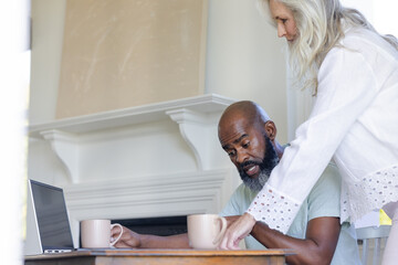 Mature couple enjoying coffee together at home, using laptop on table