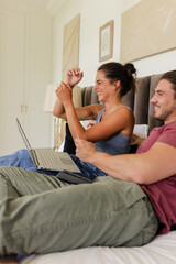Couple relaxing on bed, using laptop and laughing together at home