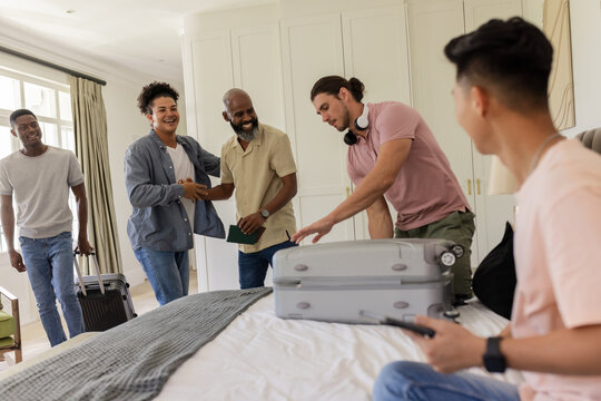 Friends gathering in bedroom, packing suitcase and sharing joyful moments together