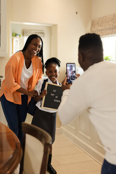 African American father taking picture of daughter holding first day of school sign
