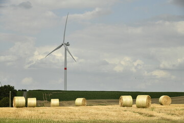 Éolienne se dressant dans le ciel derrière un champ de ballots de paille à Hellebecq (Silly)
