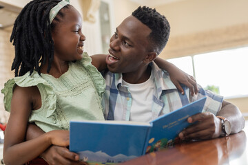 African American father reading storybook with daughter, both smiling at home