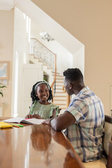 African American father helping daughter with homework at home, both smiling warmly