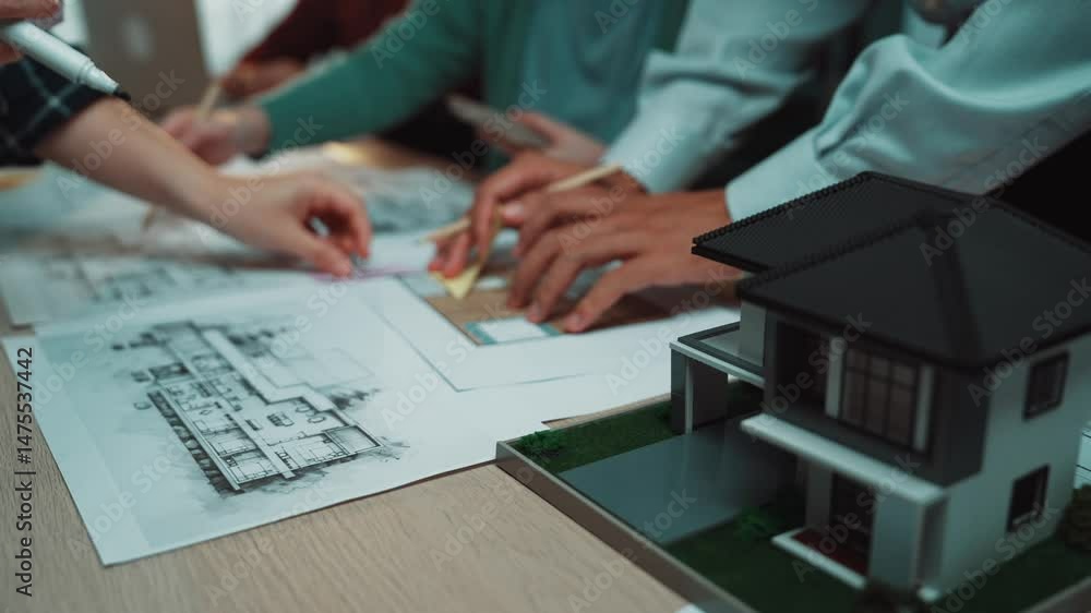 Poster team members collaborate by examining blueprints and architectural models on the table, showcasing t